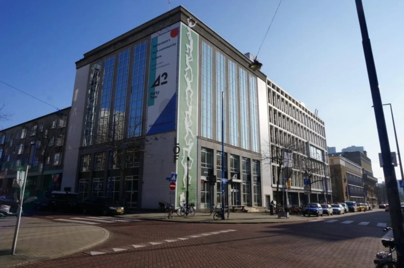 Modern building with large glass windows, featuring a colorful mural on the side, set against a clear blue sky.