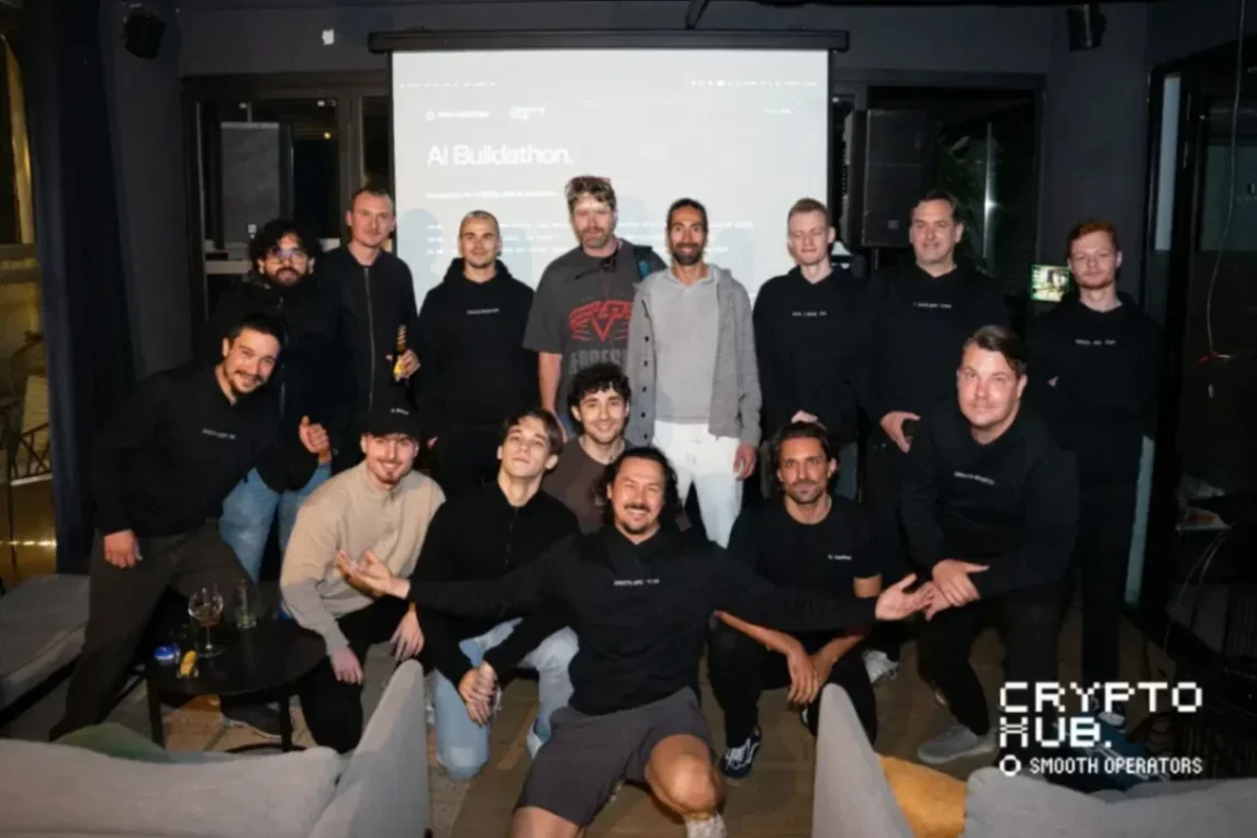 Group of people posing for a photo at an event, wearing matching black sweatshirts, in a modern space with a projector...