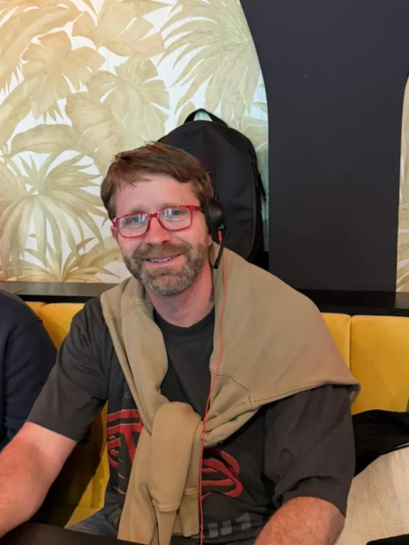 Gconf.ai's founder with glasses and headphones sitting at a table, wearing a sweater draped over his shoulders.