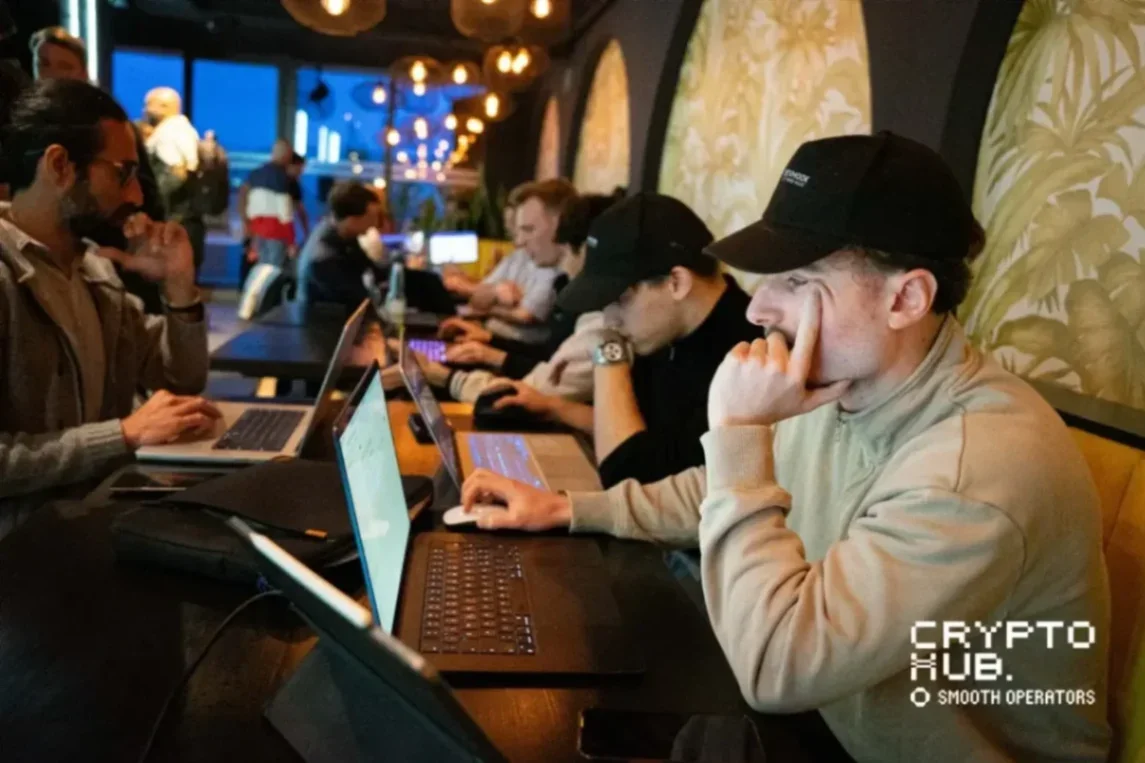A group of individuals working on laptops in a modern co-working space with ambient lighting, focused on their screens.